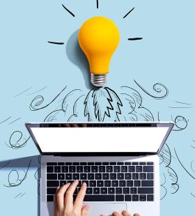 Light bulb above someone typing on a laptop.